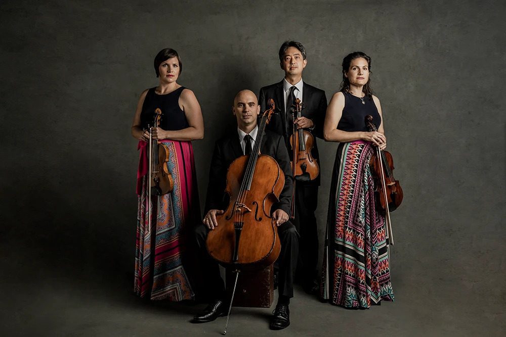 Jupiter String Quartet, posing formally with their instruments in a dramatically-lit studio photo.