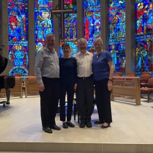 The four members of the Piano Ensemble pose in front of the church's illuminated stained glass windows.