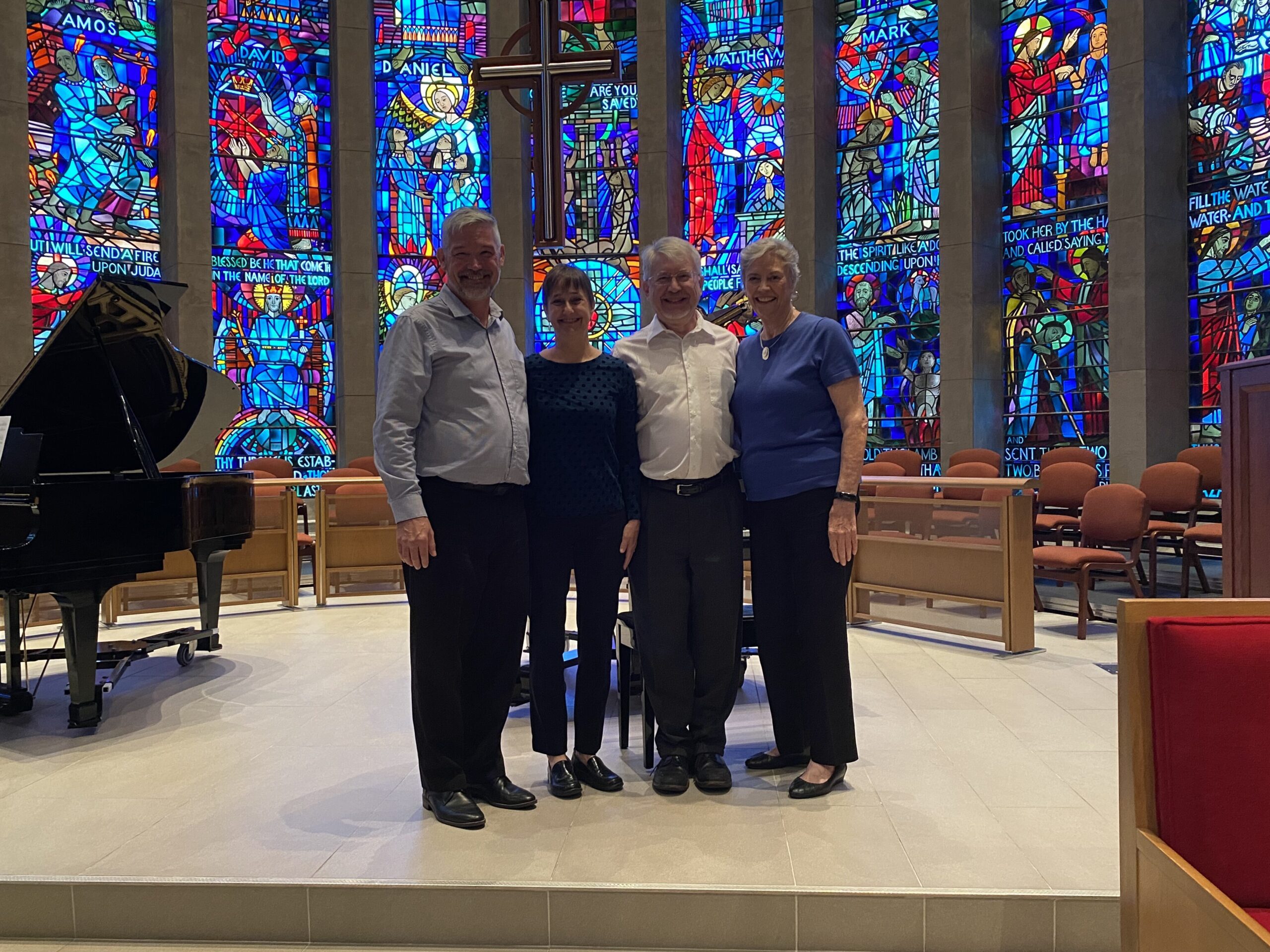 The four members of the Piano Ensemble pose in front of the church's illuminated stained glass windows.