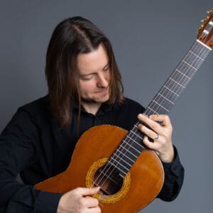 W. Mark Akin posing with his guitar in a studio setting.